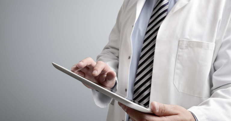 A close up of a person in a white medical coat holding a tablet device